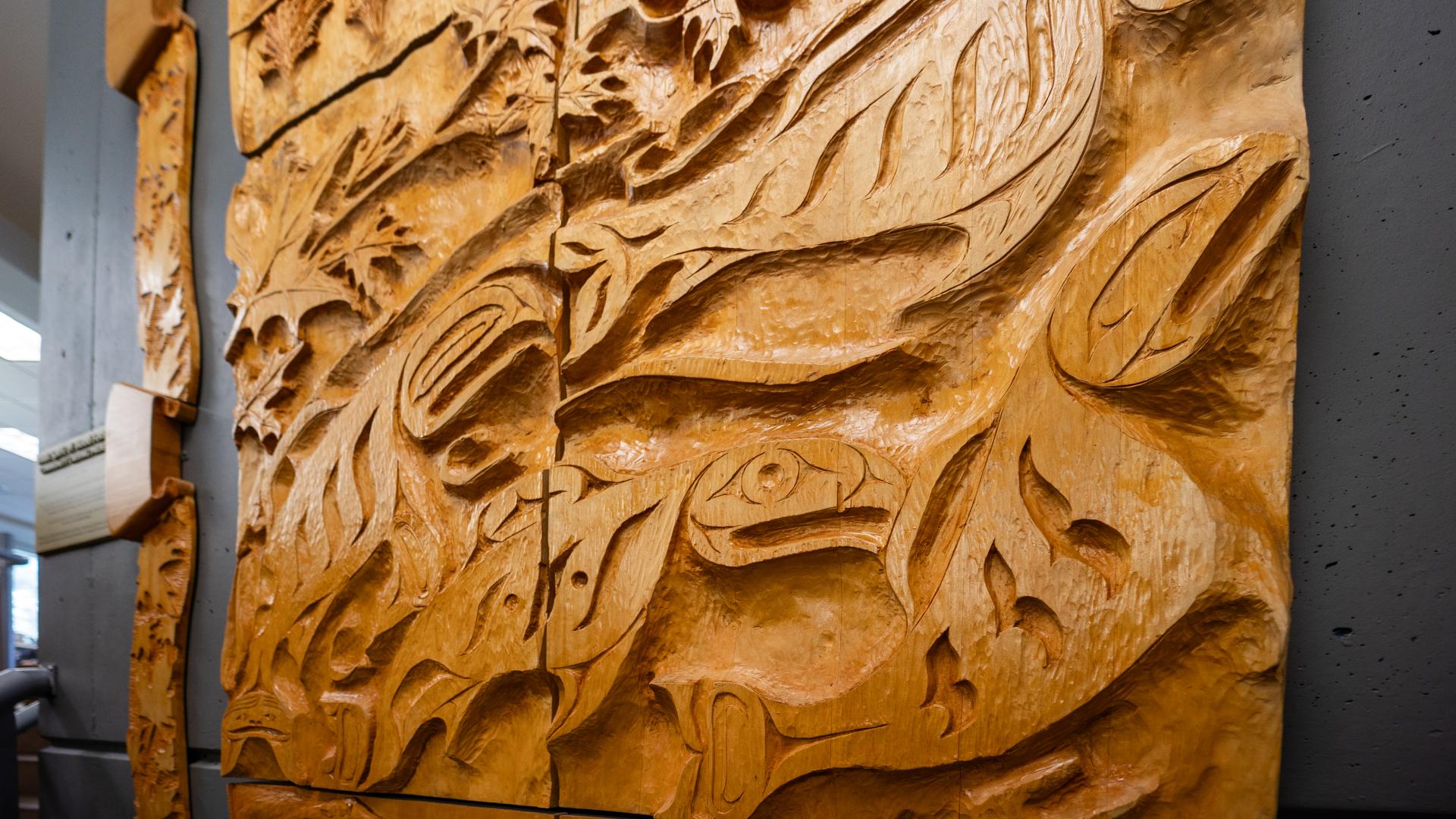 A wood carving depicting a salmon run sits on the grey wall of the Maple Ridge Library on the back of the elevator shaft.